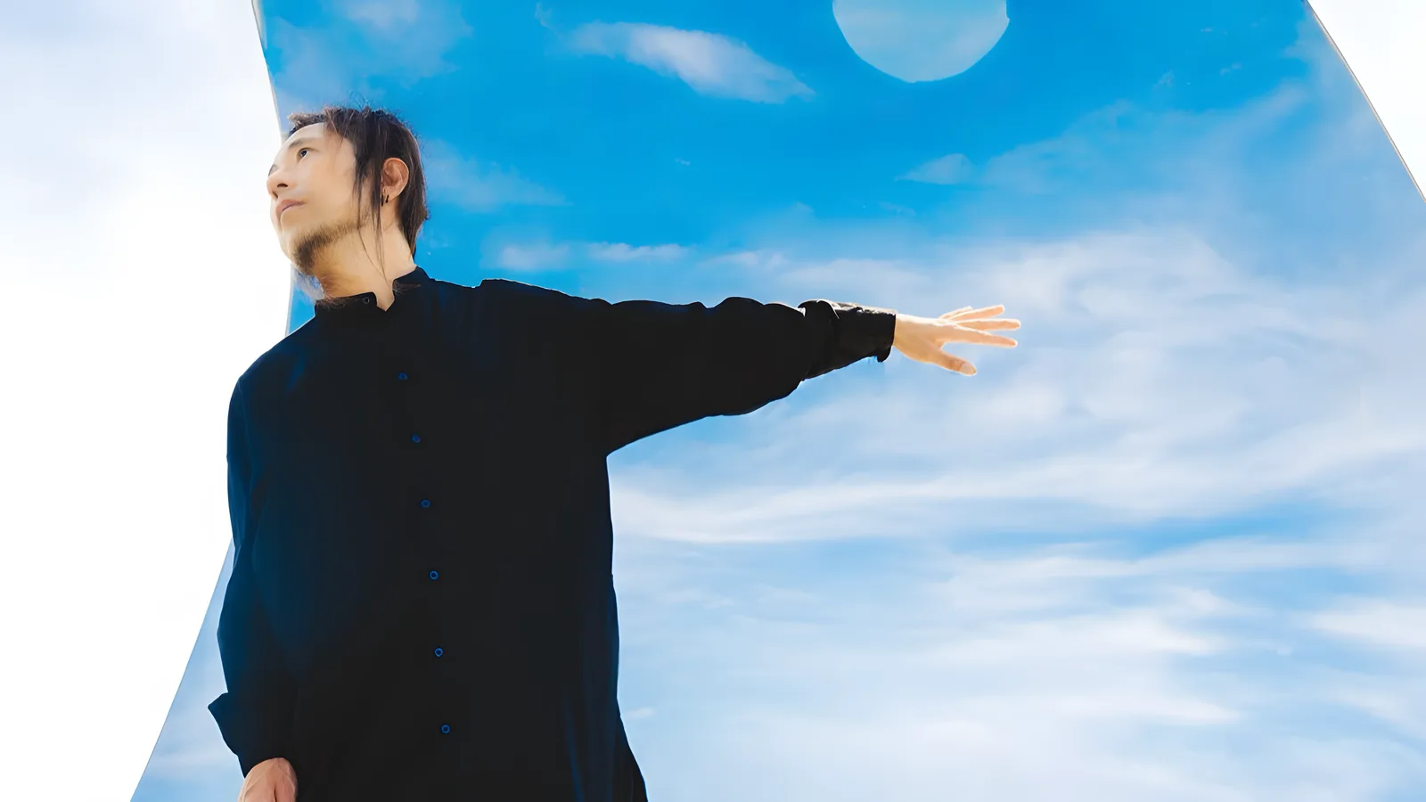 Foto promocional de ADAM at: el pianista, vestido de negro, extiende un brazo frente a un cielo azul con nubes