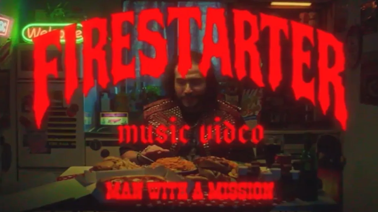 Avance del video de «Firestarter»: un integrante de MAN WITH A MISSION sentado frente a una mesa llena de comida, en un local con letreros de neón, con el título de la canción en letras rojas
