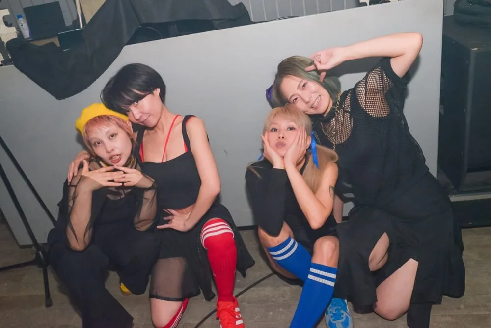 Foto promocional de NI-HAO!!!!: las cuatro integrantes posan agachadas en un club