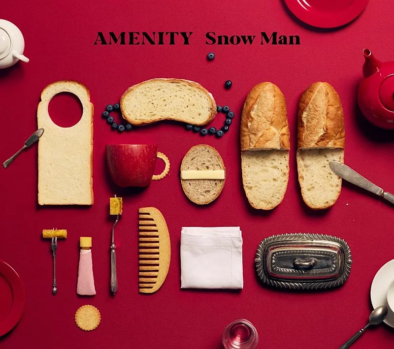 Portada del álbum AMENITY de Snow Man: panes, cubiertos y objetos de hotel acomodados sobre un mantel rojo